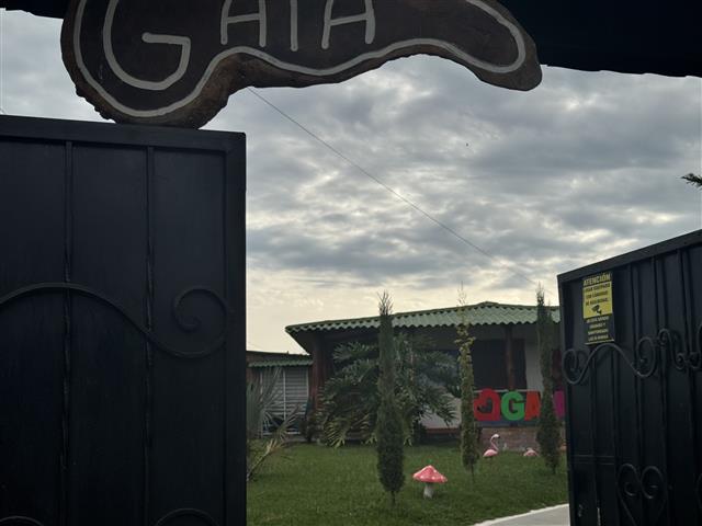 eco-hotel-gaia-10 - Hoteles en el Quindío Eje Cafetero, Alojamientos, Alquiler de fincas Open wrought-iron gate opening to a small garden with green lawn and a colorful 'GAIA' sign in the background.
