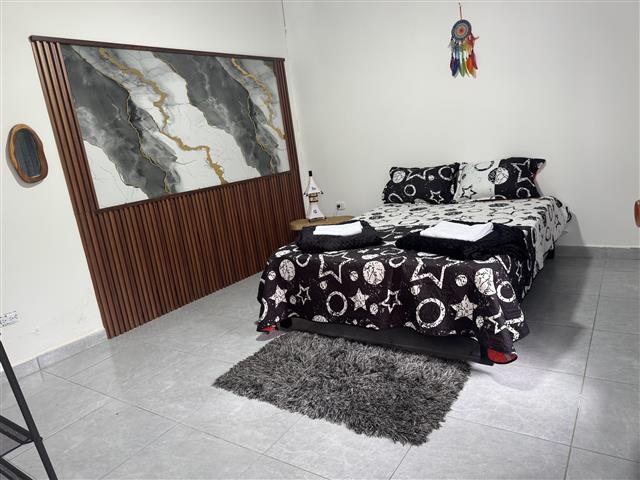 eco-hotel-gaia-13 - Hoteles en el Quindío Eje Cafetero, Alojamientos, Alquiler de fincas Double bed with black-and-white star-pattern bedding and folded towels, a gray shag rug, dreamcatcher on the wall, and a wooden headboard panel leaning against the wall.