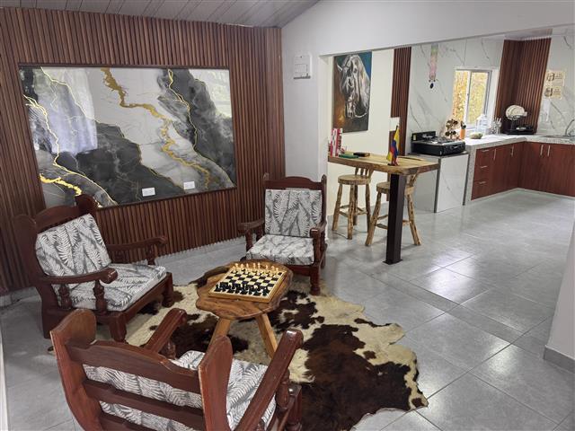 eco-hotel-gaia-16 - Hoteles en el Quindío Eje Cafetero, Alojamientos, Alquiler de fincas Cozy seating area with four wooden chairs around a small chessboard on a wooden table, atop a cowhide rug, and abstract wall art nearby.