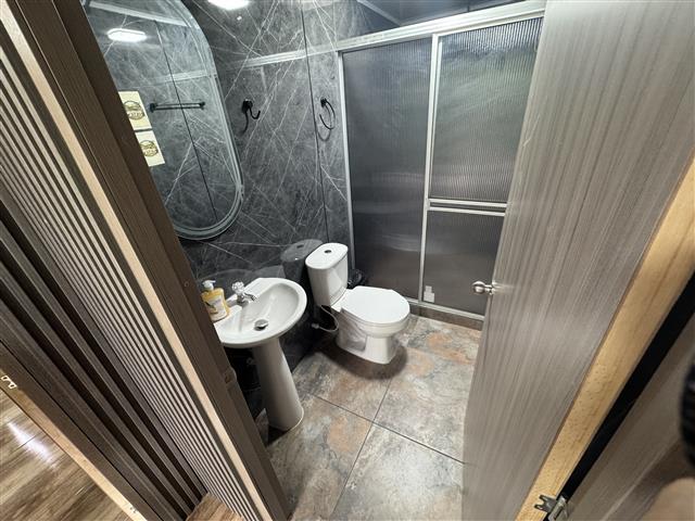eco-hotel-gaia-17 - Hoteles en el Quindío Eje Cafetero, Alojamientos, Alquiler de fincas Compact bathroom with pedestal sink, toilet, and a frosted glass shower enclosure with sliding doors, grey tiled walls and floor