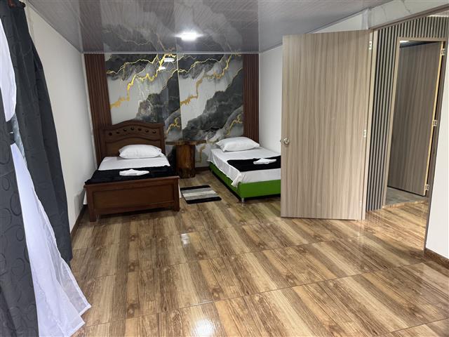 eco-hotel-gaia-20 - Hoteles en el Quindío Eje Cafetero, Alojamientos, Alquiler de fincas Hotel room with two single beds, a wooden-bed on the left and a white bed with a green frame on the right, marble-pattern wall behind, wooden floor, and an open doorway to an adjoining space.