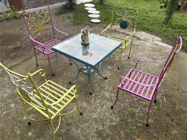 eco-hotel-gaia-8 - Hoteles en el Quindío Eje Cafetero, Alojamientos, Alquiler de fincas Colorful metal patio set with pink, yellow, and blue chairs around a glass-topped table in a backyard garden.
